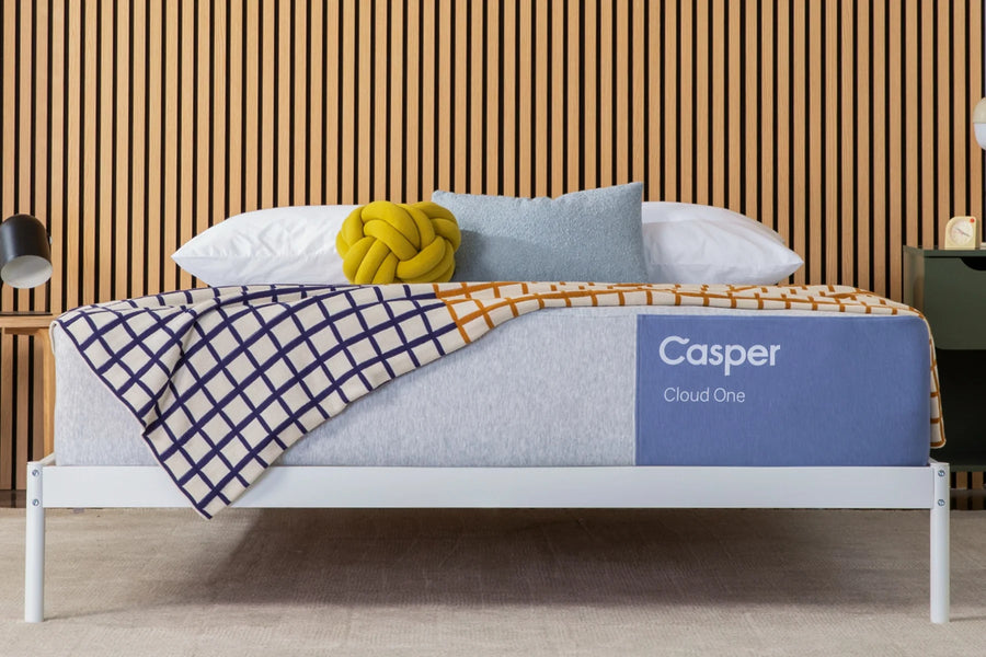 Casper bed with a plaid blanket and pillows against a wooden paneled wall.